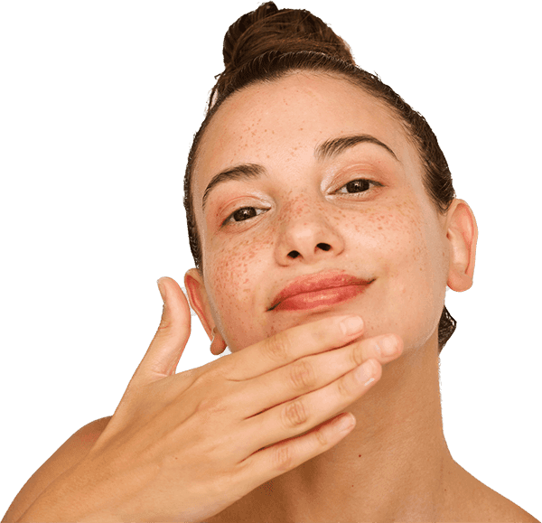 Mujer con pecas y pelo en el moño tocándose la barbilla con la mano y sonriendo ante la cámara