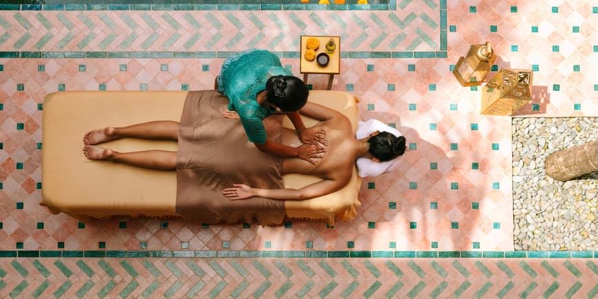 Fotografía aérea de una mujer anónima recibiendo un masaje balinés en un hermoso spa de día. Combinación de colores pastel.