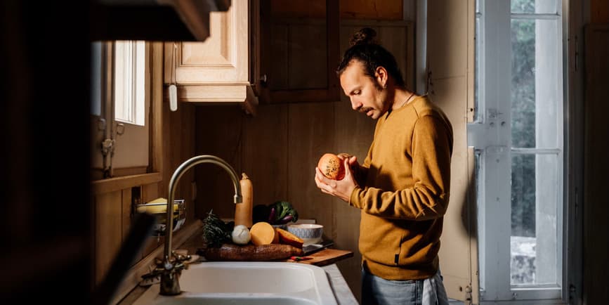 Man cooking in kitchen Man cooking healthy food at rustic kitchen home during cloudy day. Kitchen is vintage and rustic and dark. He is preparing and cooking vegetables