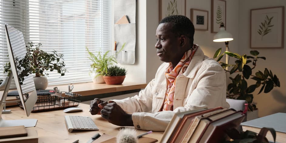 Man at computer Horizontal medium portrait of handsome young African American man wearing fashionable clothes sitting at desk at home looking at computer screen.