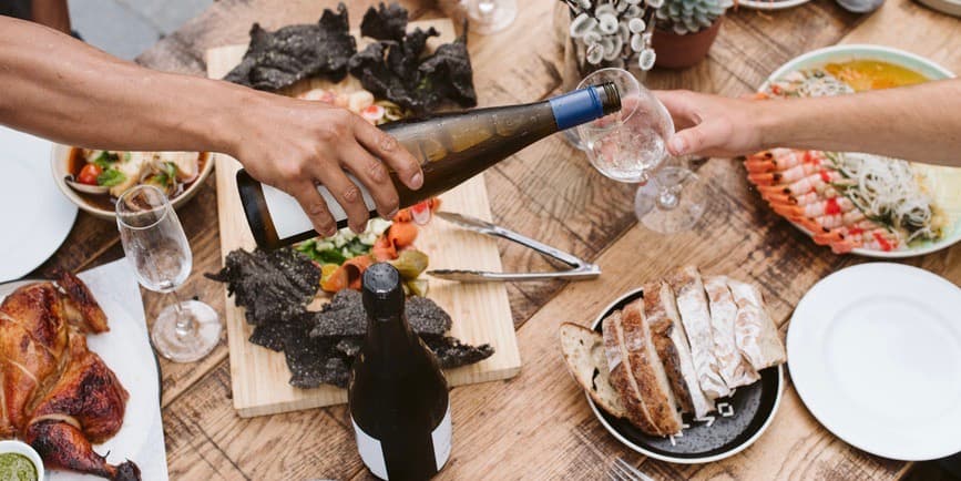 Overhead shot of full dining table An overhead photo of a brown arm pouring wine above a table set with colorful, healthy food and the suggestion of friends sitting and enjoying a meal together.