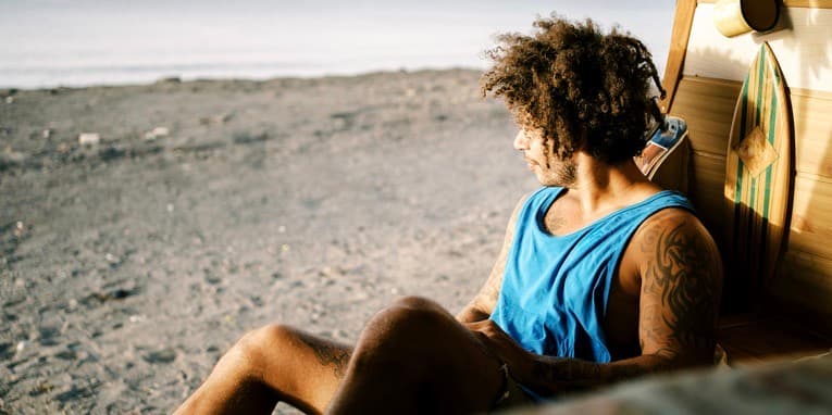 Man sitting in van at beach Side view of young hipster guy with Afro hairstyle sitting inside camper van and enjoying seascape while chilling alone at summer vacation on beach