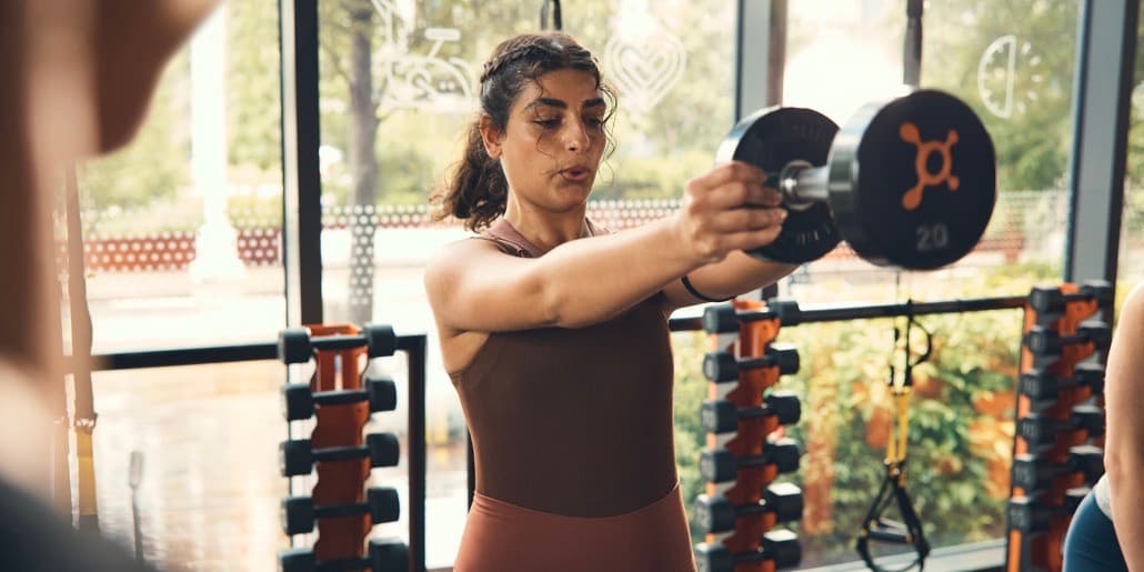 Una mujer joven se concentra mientras levanta un peso pesado durante una clase de Orangtheory Fitness.
