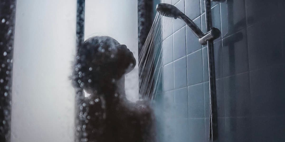 Woman in shower A steamy photo taken from the outside of a shower looking into a brown-skinned woman who stands with her face up to the flowing shower head.