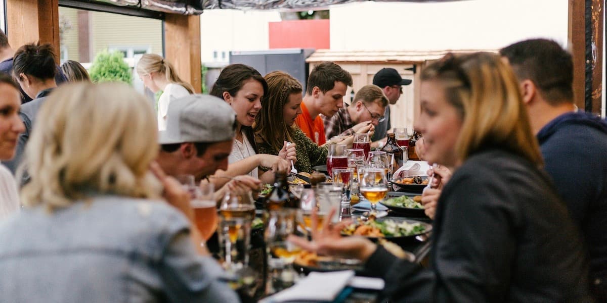 Una mesa común afuera en un restaurante repleto de gente hablando y comiendo.