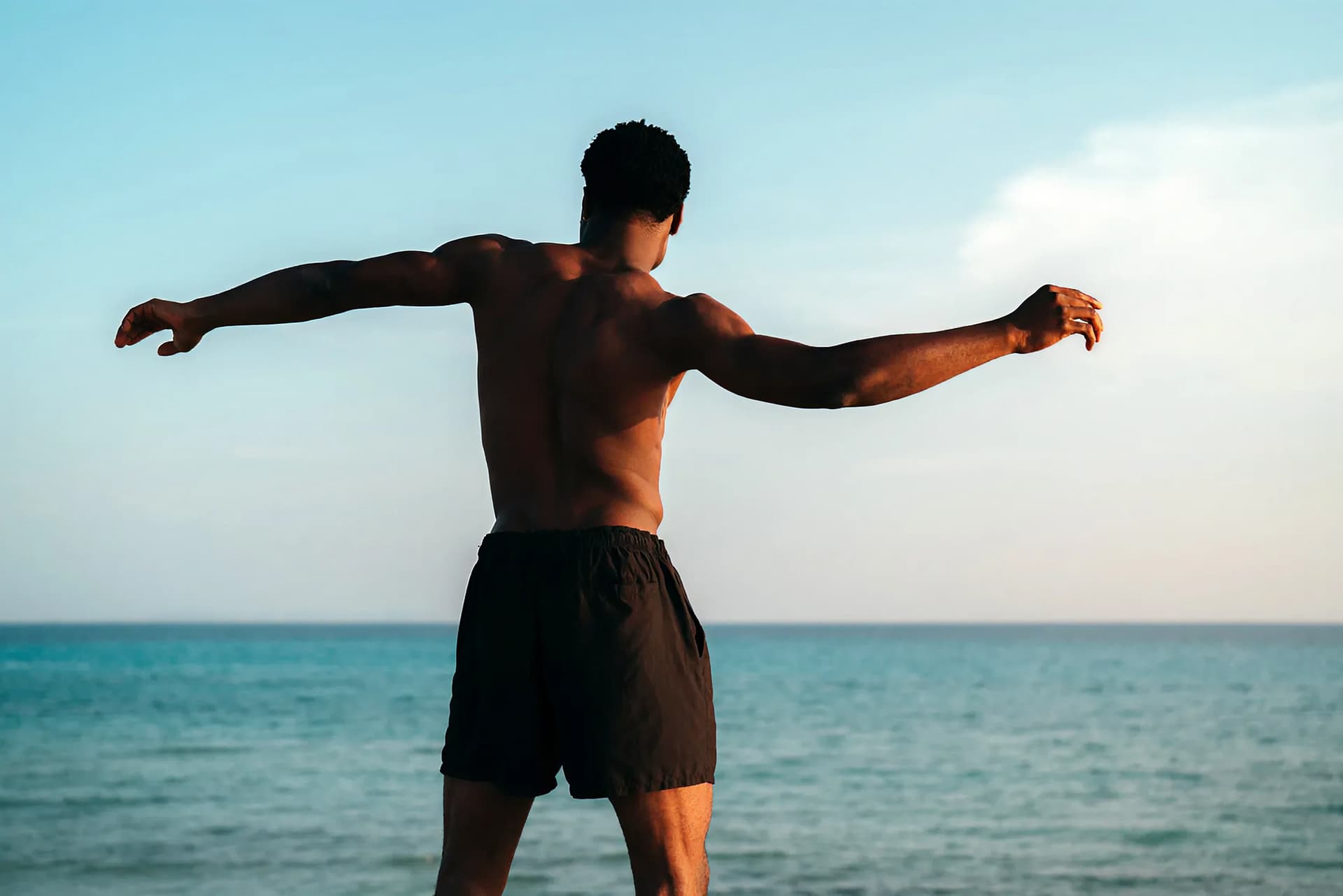 Hombre en la playa con los brazos extendidos, lo que refleja la fuerza física, la claridad mental y el bienestar general.