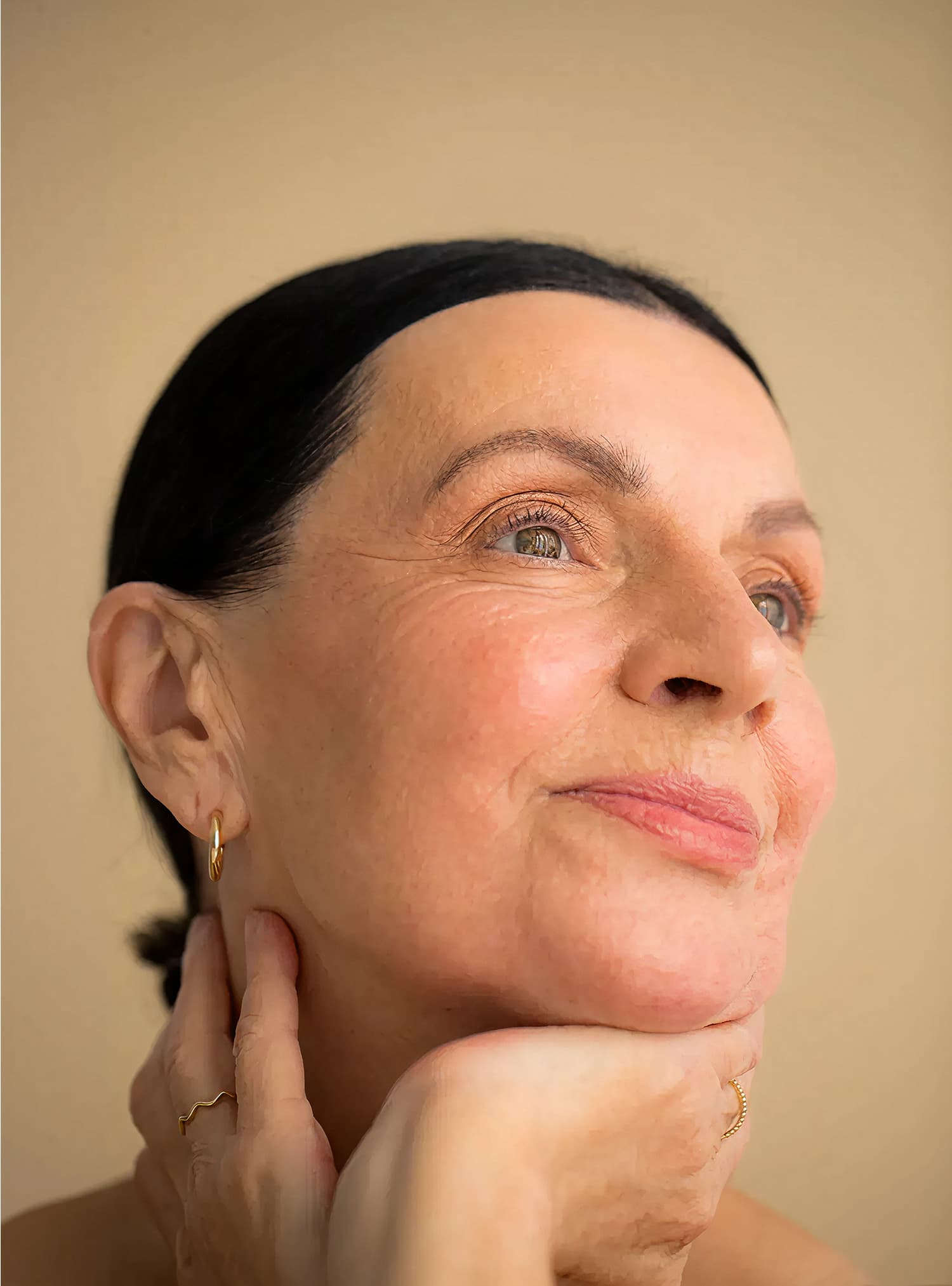 La mujer mira pacíficamente hacia arriba con una expresión serena, con las manos apoyadas suavemente sobre su cuello, resplandeciendo con calma y vitalidad